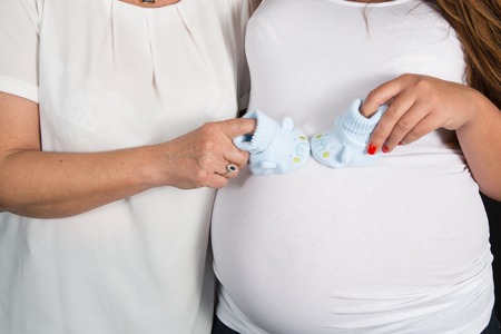 Newborn baby booties in parents hands. Pregnant woman belly.