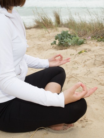 Woman meditating on the beach sitting on sandの写真素材