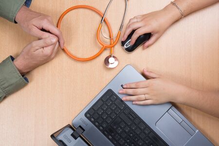 Doctor sitting at office desk and working on his laptop receiving patient