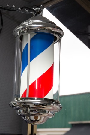 American barber pole sign with a helical stripe (red, white, and blue ) on a wall of a Barber's shop.の写真素材