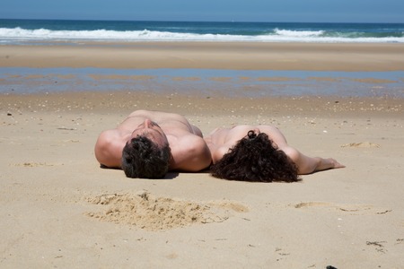 man and woman lying nude on the beachの写真素材