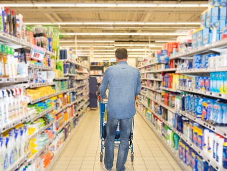 Man pushing shopping cart full of food in the supermarket aisle.の写真素材