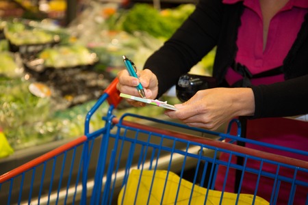 Image of woman looking at product list with goods in cart near by