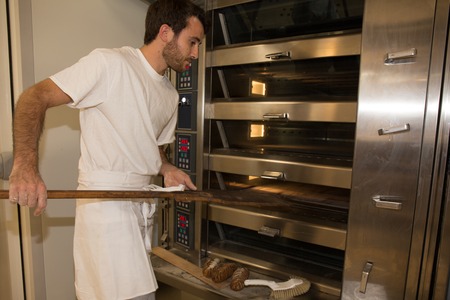 Baker in uniform taking out with shovel freshly baked bread