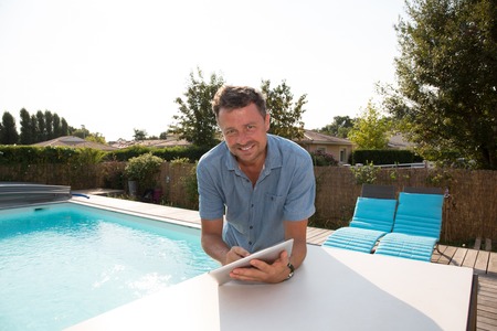 Handsome man standing by the pool smiling with digital tabletの写真素材