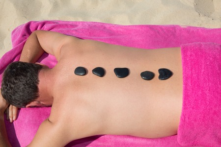 Man relaxing with hot stones on back before massage at beachの写真素材