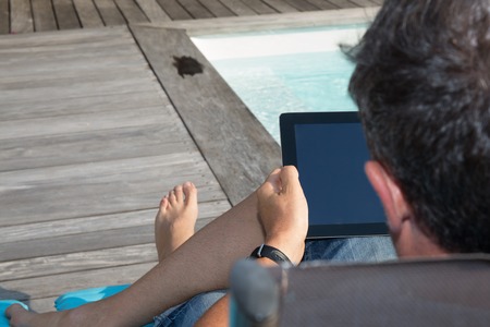 Back of a man sitting by pool with a digital tabletの写真素材
