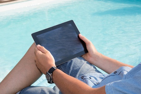 Man sitting by pool with a digital tabletの写真素材