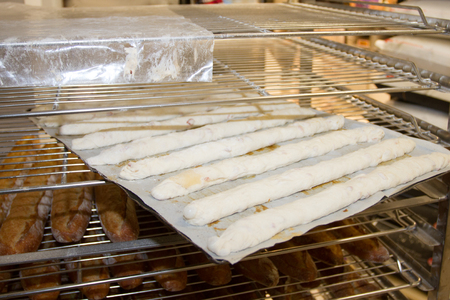 Shelves with baked and uncooked French baguettes at bakery display