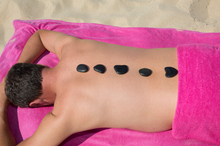 Young man relaxing with hot stones on back before massageの写真素材