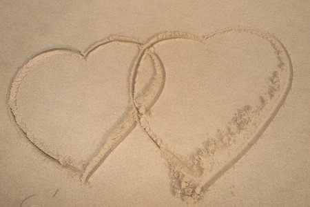 Two connected hearts drawn on wet sandの写真素材