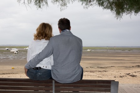 Couple sitting on the bench on the coast with the sea in the backgroundの写真素材