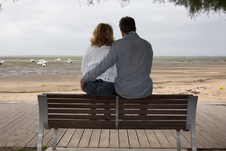 Couple sitting on the bench with the sea in backgroundの写真素材