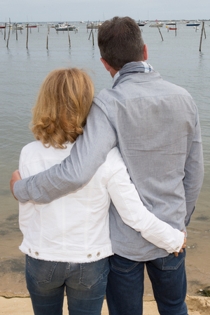 Back view of a couple hugging and watching the sea on the beach at sunsetの写真素材