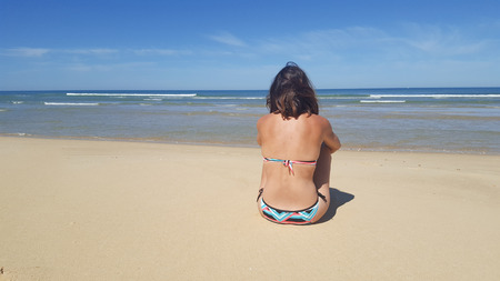 Young woman sitting on the beach relaxing at tropical resort. View from behind