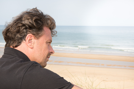 Unhappy man thinking sitting in front of the seaの写真素材