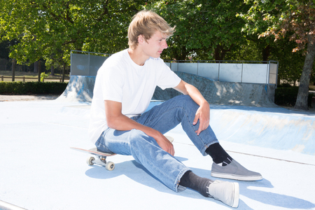 young blond man with skateboard in townの写真素材