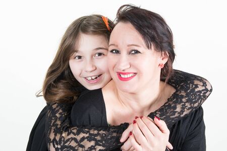 cute little daughter is hugging her charming middle-aged mother while standing together and sharing their love looking camera with smile in white backgroundの写真素材