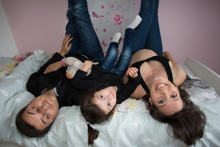 Young family is resting at home on bed pregnant mother little girl daughter and fatherの写真素材