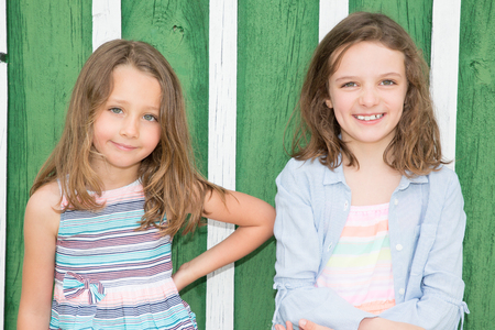 portrait of two smiling kids on green wood background Cheerful child sister happy togetherの写真素材
