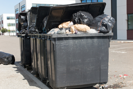 three big gray bins in the street full and overflowing with garbage bagの写真素材