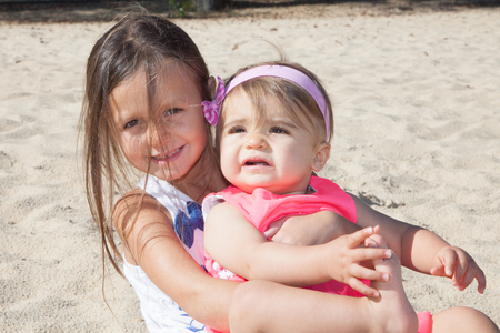 Cheerful little girl hugging in the sand beach two children sister vacationの写真素材