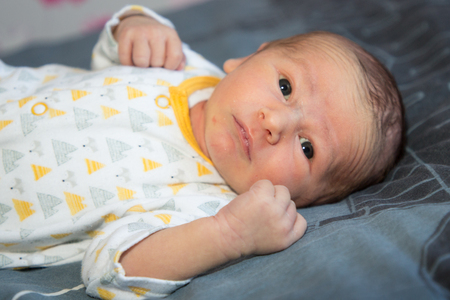 Cute cheerful newborn baby boy on grey fur blanketの写真素材