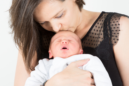 Young mother kissing sleeping her little newborn babyの写真素材