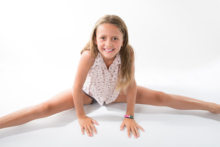 lovely little girl sitting on the floor do the split isolated on white backgroundの写真素材