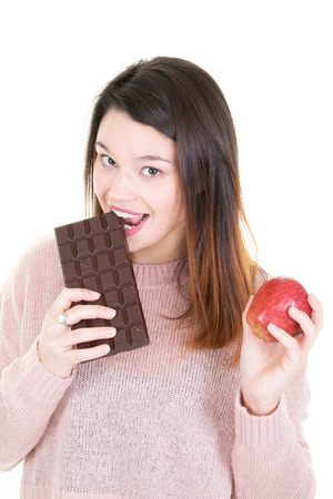 Woman holding a red apple and eating bar chocolateの写真素材