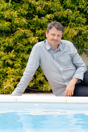 man in jeans sitting on edge floor by the swimming pool at homeの写真素材