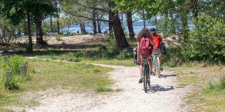 two young girls teenagers friends on bike ride in Lacanau lake sand beach in web banner template on summer dayの写真素材