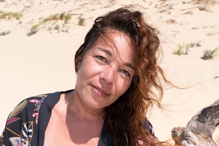 pretty middle aged woman curly hairs in wind in sand beach summer vacation