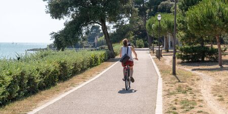 young woman on bike ride in summer day in La Rochelle city in France in web banner templateの写真素材