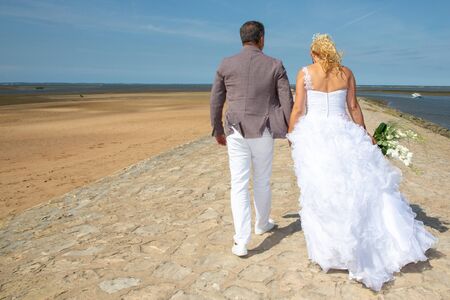 Beautiful wedding couple walking on beautiful beach in romantic sceneの写真素材