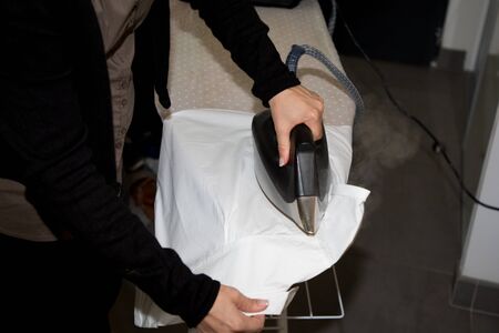 hand detail portrait of young beautiful woman with iron ironing man shirt clothesの写真素材