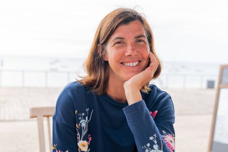 tourist woman sit at beach cafe table looks at the ocean smiling happinessの写真素材
