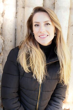 Young blonde fashion woman in black jacket posing smiling in city streetの写真素材