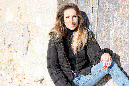 woman pretty blonde in black jacket leaning on wall sitting on streetのeditorial素材