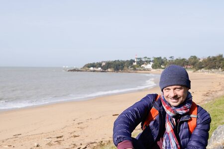 Young man standing on winter beach sea in woolen cap