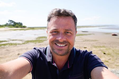 Man on vacation smiling at the beach taking selfieの写真素材