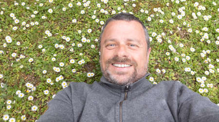 Man with beard enjoys spring in green meadow background Guy taking selfie photo on smiling face...