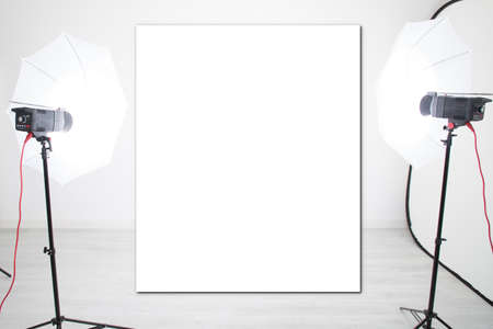 mockup empty blank white poster and studio lights on tripod stands in background with modern lighting equipment for professional photographerの写真素材
