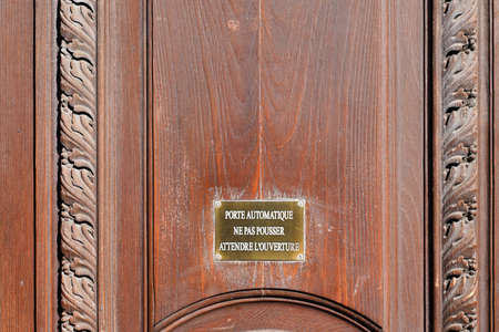 automatic door do not push wait for opening french text means automatic door do not push wait for opening accident prevention signs on wooden building doorの写真素材