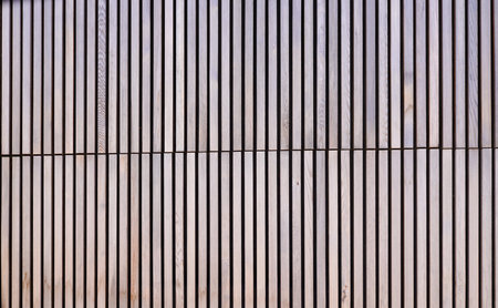 brown wooden background with wall of small vertical wooden boards on a horizontal facade in two...