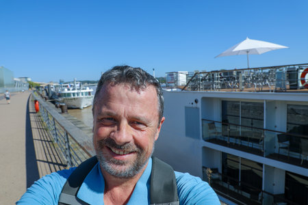 happy handsome man taking selfie with mobile phone with backpack hiking aside river in bordeaux city