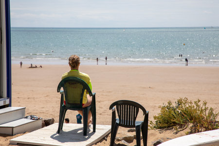 Rear view of a male lifeguard dutifully watches over swimmers in atlantic ocean beach safety careの写真素材