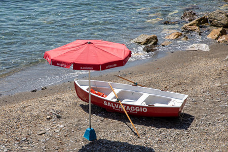 Genoa, Italy - 08 19 2024: lifeguard salvataggio red umbrella and wooden boat sign text italian bagnino means lifeguard rescue at Genoa beach italyのeditorial素材