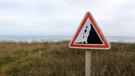 Traffic sign falling rocks on iron panel located along seacoast cliff