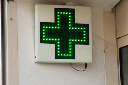 large neon green cross pharmacy light sign medical symbol on facade of shop buildingの写真素材